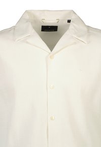 Camisa de lino blanca de manga corta con cuello puntiagudo, cinco botones y un sutil logo bordado en el pecho. Tejido suave y texturizado.