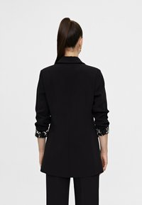 Czarna, dopasowana marynarka z kołnierzem, podwiniętymi rękawami ozdobionymi wzorzystym mankietem oraz klasycznym krojem zapewniającym uporządkowany fason.