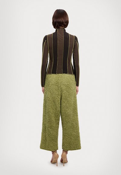 Haut marron ajusté avec des rayures verticales et un col montant, associé à un pantalon vert ample et texturé. Le modèle porte des talons beiges.
