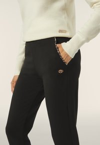 Pantaloni neri su misura con tasche laterali, dotati di una fodera con stampa leopardata e un accento dorato sul taschino. Tessuto morbido.