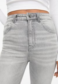Grå højtaljede jeans med en falmet vask, fem lommer, knap- og lynlåslukning samt synlige syninger. Glat tekstur.
