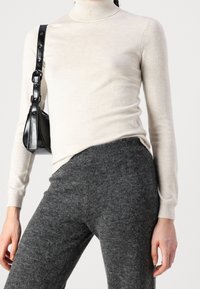 Krémový rolák se dlouhými rukávy, kombinovaný s tmavě šedými, měkkými vlněnými kalhotami. Černá crossbody taška s accenty ve tvaru knoflíků.