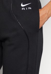 Svarta sweatpants gjorda av mjukt tyg, med vit "Nike AIR"-logotyp, slank design och kontrasterande sid sömmar för extra detalj.