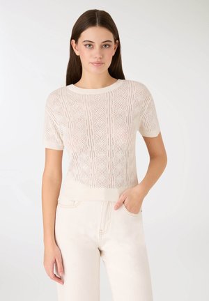 Maglione corto a maniche corte color crema lavorato a maglia con motivo a diamante e trama, scollo e orlo a coste. Il modello lo abbina a denim di colore chiaro.