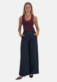 Bordeaux tanktop met contrasterende naden, gecombineerd met hoge, brede, zwarte broek met plooien en zijzakken.