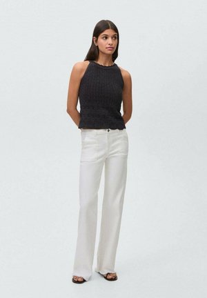 Black knitted halter top with textured pattern, paired with white wide-leg trousers. Model stands against a light background.