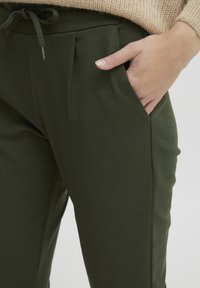 Groene joggers van katoenmix met een taillekoord, zijzakken en plooien aan de voorkant voor extra detail. Glad textuur.