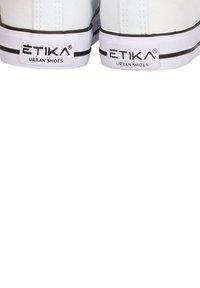 Zapatillas de lona blancas con detalles negros en la suela, que cuentan con una etiqueta de logo que dice "ETIKA URBAN SHOES" en el talón.
