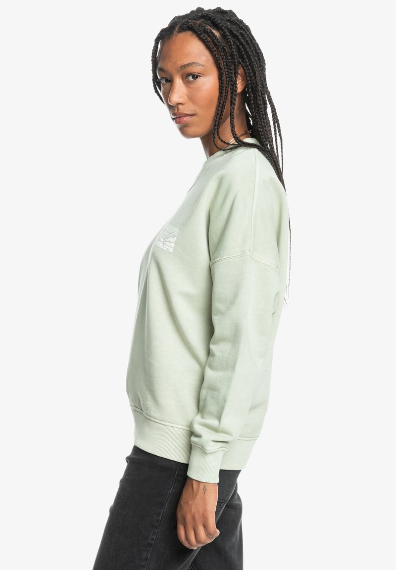 Helles grünes Sweatshirt mit langen Ärmeln, gerippten Bündchen und Rundhalsausschnitt. Verfügt über eine kleine weiße Grafik im linken Brustbereich.