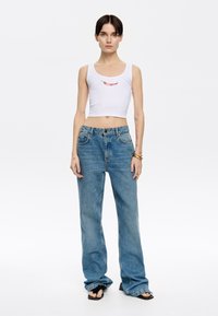 Witte geribde crop top met een rode chili graphic, gecombineerd met losse blauwe jeans met een klassiek vijf-pocket ontwerp en rafelige zoom.