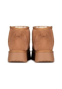 Botas de tobillo de ante marrón con un acabado texturizado, forro de piel de pelo suave y suela de goma. Incluyen una pestaña en la parte trasera para facilitar su uso.
