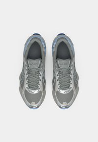 Ténis desportivos cinzentos com parte superior em rede, detalhes reflexivos e sola azul. Apresentam atacadores e interior almofadado para suporte.