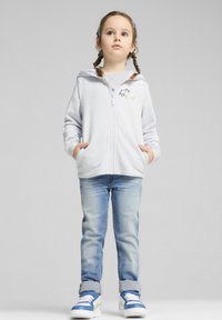 Felpa zip grigia chiara con tasche frontali, abbinata a jeans blu e sneakers blu con dettagli bianchi e verdi.