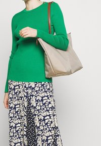 Vihreä ribbineulottu neulepusero pyöreällä pääntiellä ja napillisin yksityiskohdin, yhdistetty kukalliseen ja pilkulliseen hameeseen. Beige kylmälaukku ruskealla hihnalla.