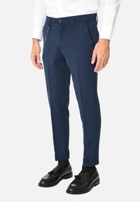Pantaloni tailored blu navy con una vestibilità slim, dotati di un'accento laterale in catena, tessuto liscio e chiusura a bottone in vita. Abbinati a mocassini neri.