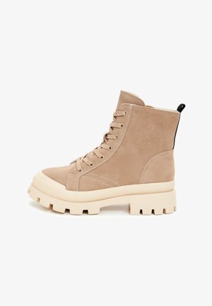 Cizme ankle din suede bej, cu o suprafață texturată, vârf rotund, șireturi în față și o talpă solidă albă, groasă. Punct de prindere negru în partea din spate.
