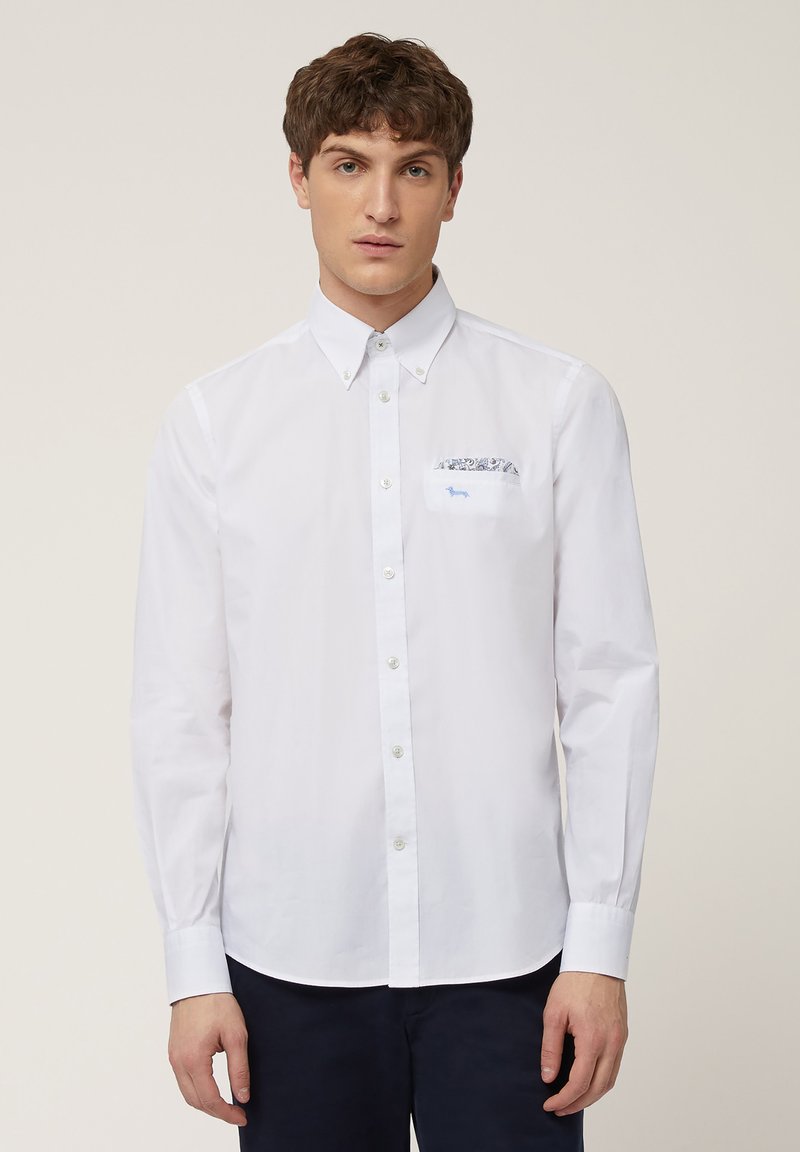 Chemise blanche à boutons avec un col pointu, dotée d'une poche poitrine à motif et de manches longues. Tissu lisse, coupe classique, design minimaliste.
