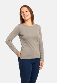 Top a maniche lunghe, collo tondo, in morbido tessuto beige, dal design aderente, con dettagli di cucitura minimi. Abbinato a jeans blu scuro.