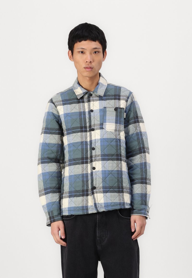 Gequilted flanellen jack in blauw, grijs en wit geruit, met een knoopsluiting aan de voorkant, één borstzak en een ontspannen pasvorm. Plat kraagontwerp.