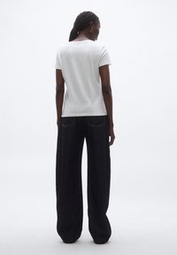 Fehér pamut póló kerek nyakkivágással, lazán szabott sötét farmernadrággal, egyenes szabással és két hátsó zsebbel.