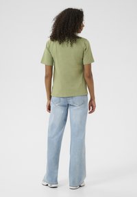 T-shirt vert à manches courtes avec une coupe décontractée, associé à un jean large bleu clair et des baskets blanches. Tissu en coton doux.