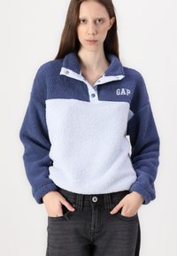 Fleece pulóver v námorníckej modrej a svetlo modrej farbe s golierom na patentky; obsahuje logo "GAP", textúrovaný povrch a voľný strih.