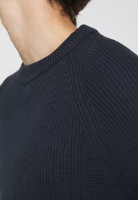 Marinblå ribbad stickad tröja med rund halsringning. Har ett strukturerat tyg och design med raglanärmar som ger en bekväm passform.