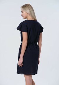 Marinblå klänning med korta volangärmar, åtsittande midja och knälång nederkant. Har en enkel design med lätt, strukturerad tyg.