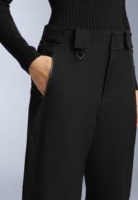 Černé kalhoty s hladkým materiálem a přiléhavým střihem, s poutky na pásek, bočními kapsami a elegantním designem. Zajímavý detail s kovovými prvky.