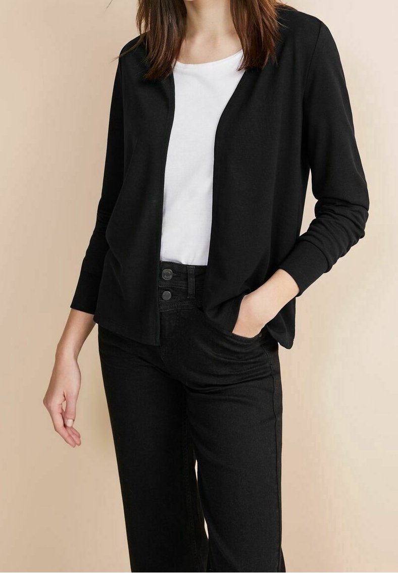 Černý lehký cardigan s otevřeným předním dílem, dlouhými rukávy a uvolněným střihem, nošený přes bílý top a spárovaný s černými kalhotami.