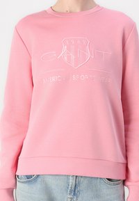 Pink sweatshirt made of soft fabric featuring a round neckline, ribbed cuffs, and a white embroidered logo with "1949" and "AMERICAN SPORTSWEAR."