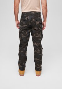 Camouflage cargo pants in dark green and black, featuring multiple side pockets, a relaxed fit, and a durable cotton blend material.