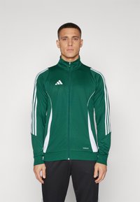 Grønn zip-up atletisk jakke med hvite detaljer og tre vertikale hvite striper på hver arm, laget av et glatt og lett stoff.