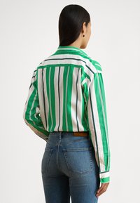 Πράσινο και λευκό ριγέ πουκάμισο με μακριά μανίκια, γιακά και μανσέτες με κουμπιά, συνδυασμένο με τζιν ψηλόμεσο μπλε. Λείο ύφασμα.