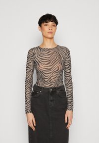 Langärmliges Mesh-Top mit einem beige-schwarzen Zebra-Muster, kombiniert mit einem hochgeschnittenen schwarzen Denim-Rock, der über Taschendetails verfügt.