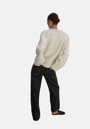 Pull crème en tricot épais avec épaules tombantes, associé à un jean noir taille haute. Chaussures noires à enfiler, au design minimal, sans motifs.