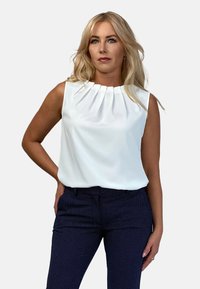 Biała bezrękawnik z plisowanym dekoltem, zestawiona z granatowymi spodniami w kropki. Gładki materiał o miękkiej fakturze, dopasowany krój.