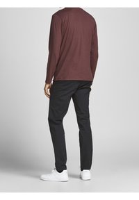 Mörkröd långärmad skjorta och svarta byxor som bärs med vita sneakers. Skjortan har en rund hals och är enkelt designad, medan byxorna är rakskurna.