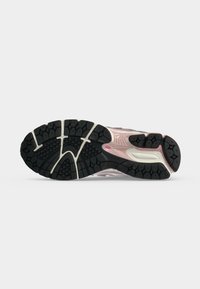 Semelle de chaussure avec motif de bande de roulement noir et blanc, détail de semelle intermédiaire rose et logo New Balance sur fond gris clair lisse.