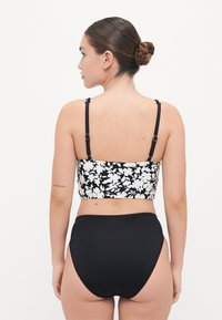 Top bikini floreale bianco e nero con spalline regolabili e culotte alte nere a tinta unita, che mettono in risalto un design aderente e una consistenza morbida.
