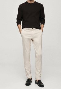 Pantalon beige clair à coupe ajustée avec une fermeture à un bouton, associé à un pull côtelé marron foncé et des mocassins noirs.