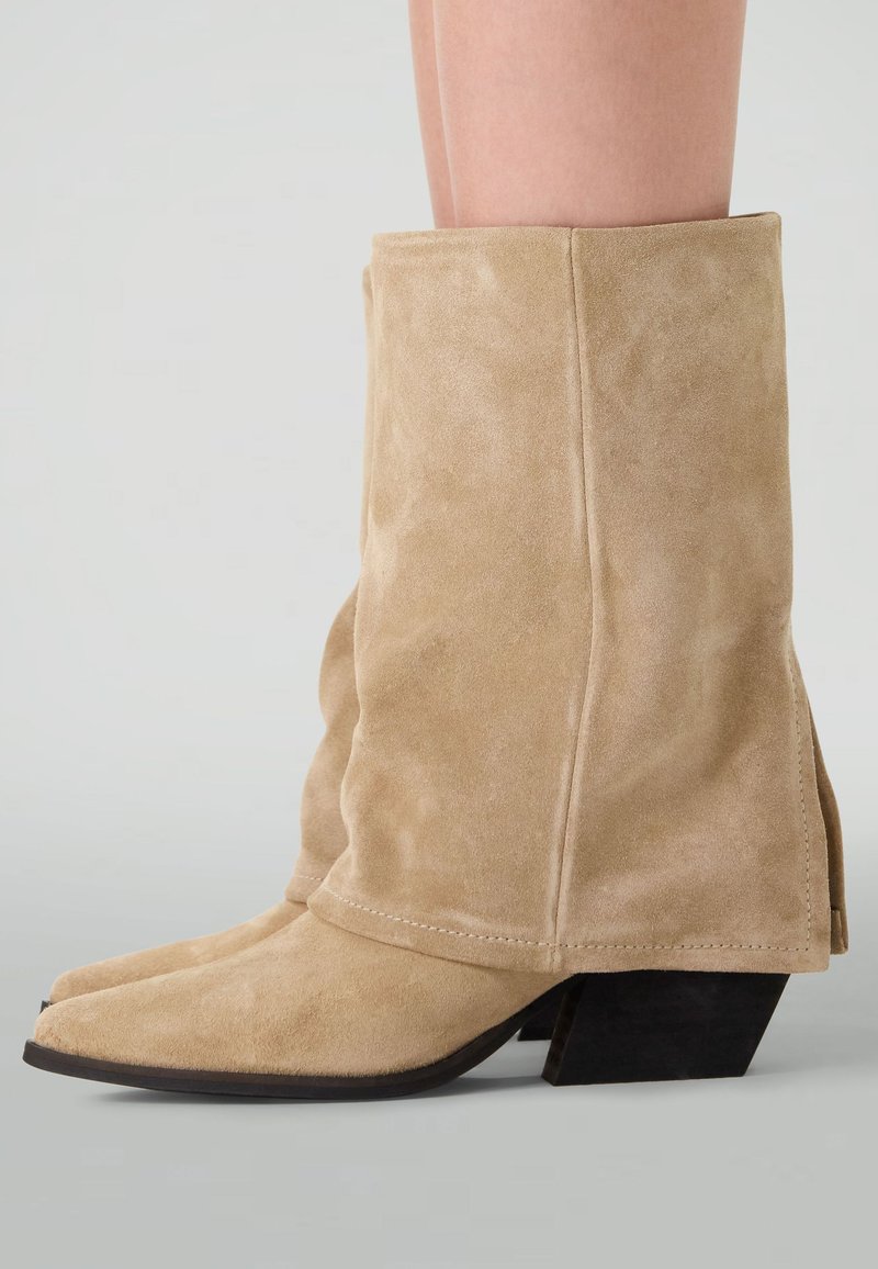 Beige suède enkellaarsjes met een slouchy ontwerp, spitse neuzen en een lage blokhak. Beschikt over stikseldetails langs de naden.