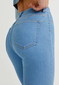 Jeans ajustados de color azul, fabricados en denim, con una cintura de altura media, bolsillos traseros y costuras visibles en un color contrastante.