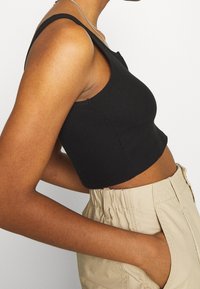 Svart ribbad croppad tanktop med breda axelremmar, kombinerad med högmidjade beiga byxor med sidofickor och elastisk midja.