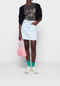 Světlé modré džíny sukně s třepeným lemem, doplněná černým svetrem přes květinově potištěné tmavé tričko. Růžová tkaná kabelka a zelené ponožky.