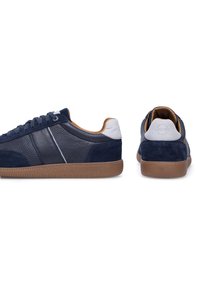 Zapatillas azul marino con cuero texturizado y detalles de ante, talón blanco, suela de goma marrón y detalle de franja lateral en contraste.