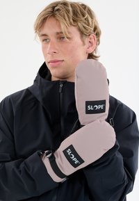 Des moufles roses avec une texture lisse, ornées d'un logo SLOPE noir et de sangles réglables au niveau des poignets, portées sur une veste sombre.