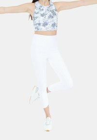 Valkoinen lyhyt urheilupaita, jossa on harmaa ja musta abstrakti kuvio, yhdistettynä valkoisiin nilkkapituisii leggings-housuihin ja vaaleanharmaisiin lenkkikenkiin.