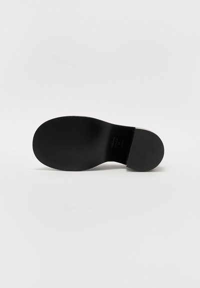 Sola di calzature nera con una texture liscia, forma leggermente arrotondata e un design minimalista. Nessun logo o motivo visibile presente.
