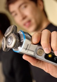 Philips elektrisch scheerapparaat met een metallic zilveren behuizing, drie ronde koppen en blauwe LED-accenten. Beschikt over een aan-/uitknop met een LED-display.